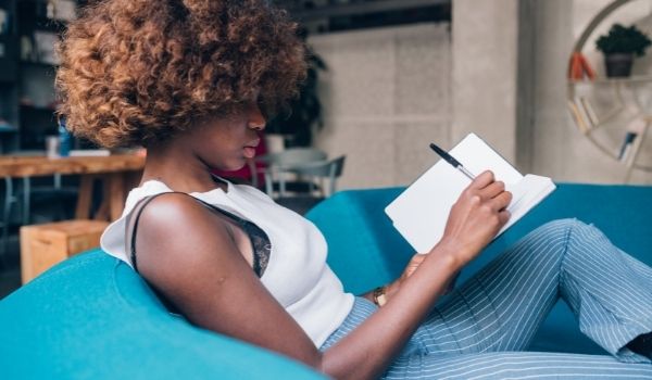 a woman lying on a sofa writing in her journal