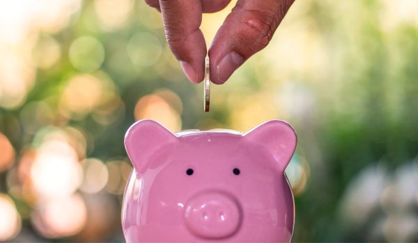 a pink piggy bank with a hand dropping a coin into it