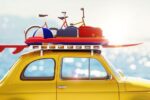 A yellow car with a surfboard and beach gear on its roof