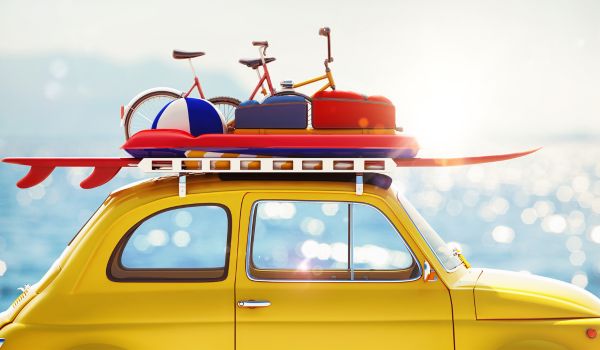 A yellow car with a surfboard and beach gear on its roof