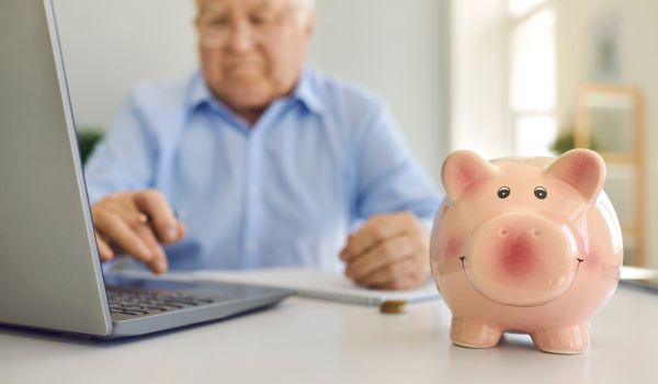 a man sitting at his computer with a piggy bank in the foreground