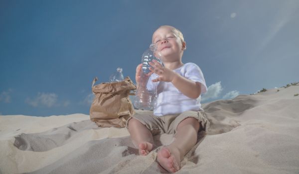 a baby taking the last sip of cold bottled water on a beach