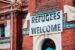 a refugees welcome sign hanging from a brick building