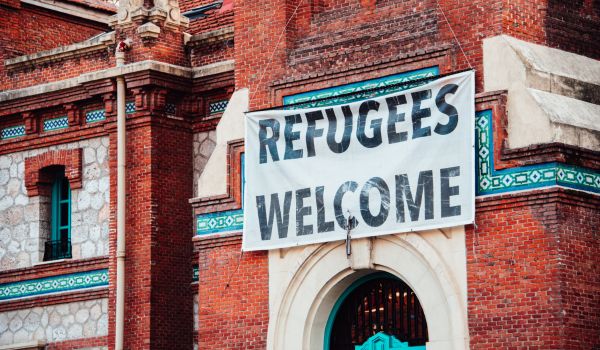 a refugees welcome sign hanging from a brick building