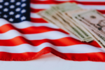An American flag with a stack of dollar bills resting on it