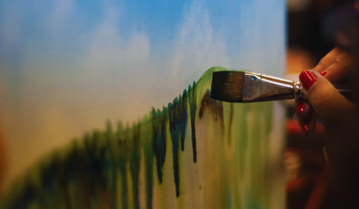 A female hand with red nails paints a green line on a canvas