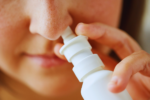 A sick woman using a flu nasal spray