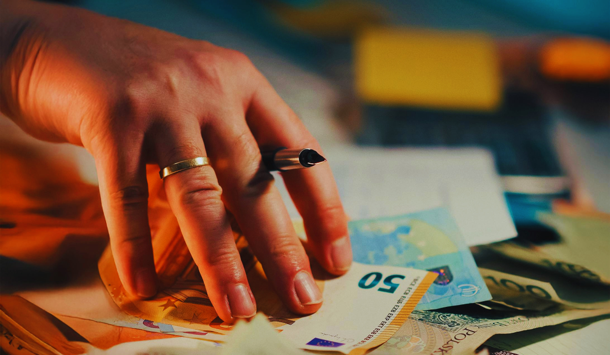 Closeup of hand with a pen and several euro banknotes
