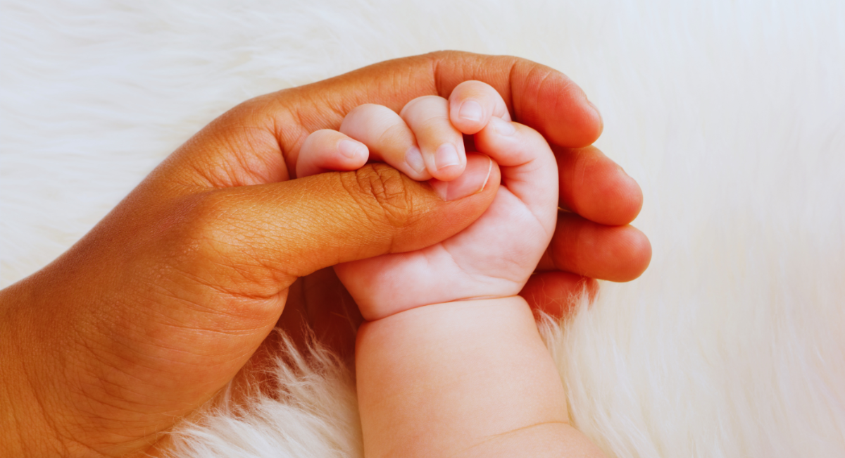 A closeup photo of a man holding a childs hand representing adoption